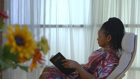 A Christian African American woman closes the Bible she is reading and moves into reverent prayer time.
