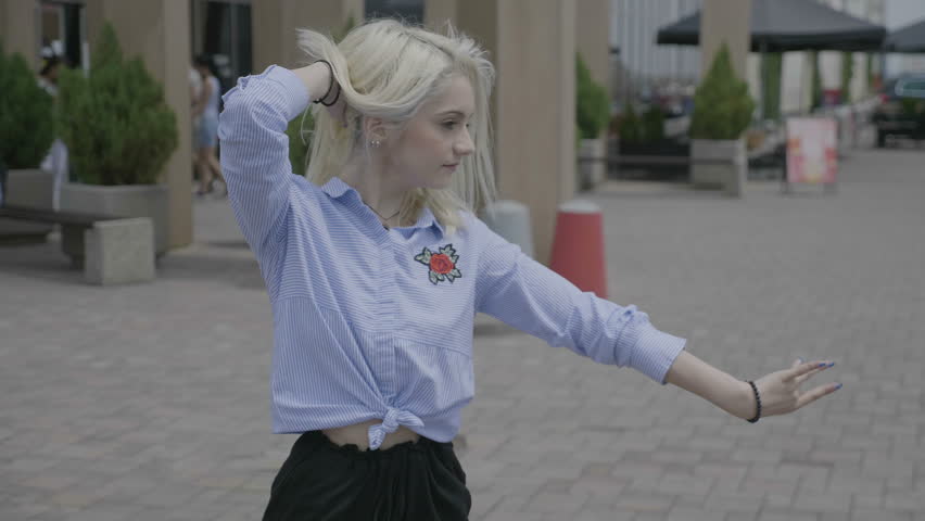Beautiful skillful young woman performing salsa dance outside in the street with urban building in city center