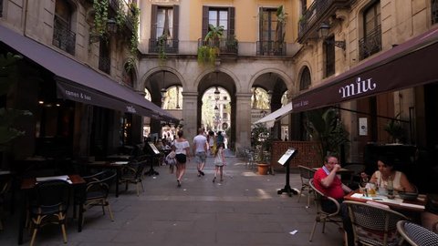BARCELONA, SPAIN - AUGUST 13, 2018: Discovering of Gothic Quarter of city, POV walk at small passage to Royal Plaza, unidentified tourist family come ahead, people rest at cafe. Lovely old city
