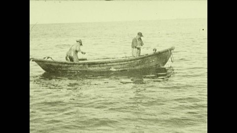 1930s: Men on rowboat pull halibut and cod into boat from trawling lines.