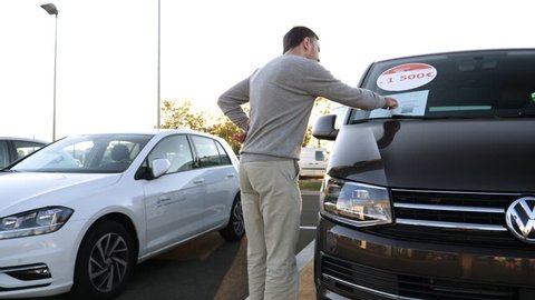 LYON, FRANCE - CIRCA 2018: Curious Caucasian young customer admiring the brown Volkswagen Vw transporter van offered by Vw Das Welt car dealer - checking the price and discounts of 1500 euros