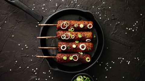 Barbecued turkey kebab decorated with fresh onion and chive in frying pan, top view. Black stone background.