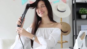 Young Beautiful Asian beauty blogger woman in white room curling her long hair with curling iron and smile. 