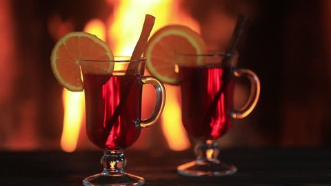 Two glasses of hot mulled wine with spices on wooden table against fireplace