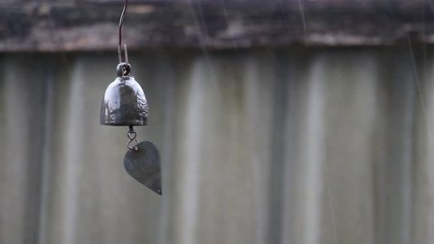 Bell or chime hanging and swaying in wind that is in the rain.