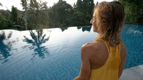 Girl making heart shape finger frame with hands when sitting on the edge of infinity swimming pool in tropical rainforest in Bali. People travel vacations love concept. 4K resolution 