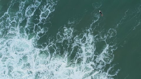 Aerial view of turquoise sea with seafoam and male surfer paddling out. Biarritz, France.