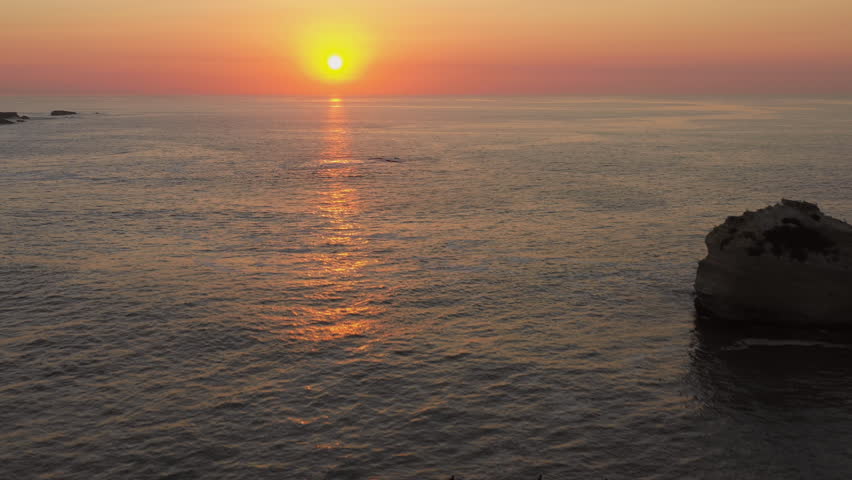 Drone shot rising above the sea. Orange sun at sunset. Atlantic Ocean, Biarritz, France.