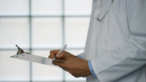 Hands of a Doctor in a hospital ward writing notes on a clipboard