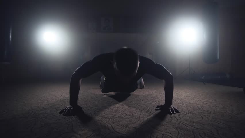 Professional boxer doing push-ups in dark smoky gym. Athlete training in elastic bandages. Sport concept in slow motion. Silhouette on dark background Royalty-Free Stock Footage #1017517624