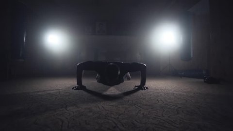 Professional boxer doing push-ups in dark smoky gym. Athlete training in elastic bandages. Sport concept in slow motion. Silhouette on dark background