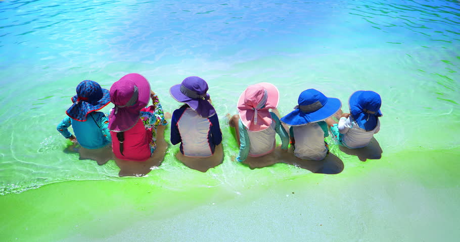 Cute little girls in hats sitting in the water having fun on the ocean sandy beach during summer vacation in Labadee, Haiti, 4K