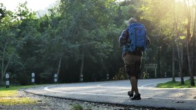 Traveler Asian men walking on road enjoying view sunset in beautiful forest landscape. Travel Lifestyle concept vacations into the wild wearing cozy shirt,hat with backpack. video 4k  Slow motion