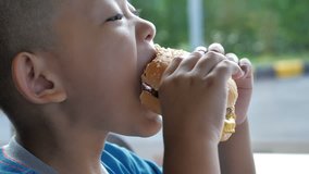 Close up little asians boy enjoy eating burger, Cute happy boy holding hamburger at restaurant. video Slow motion