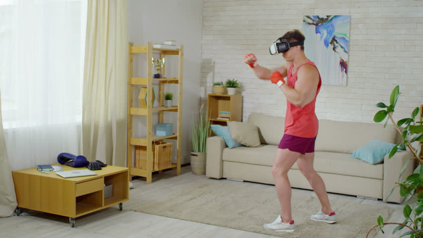 Muscular Caucasian man in VR headset boxing with holographic opponent while practicing punches in the living room Royalty-Free Stock Footage #1017528628