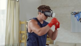 Sporty man in VR glasses with physical activity metrics and timer practicing punches in holographic wall projected in the living room while training at home