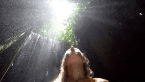 Young woman in tropical rainforest looking up at beautiful light and touching the rain drops with hands. People travel enjoying nature and life concept. Slow motion video