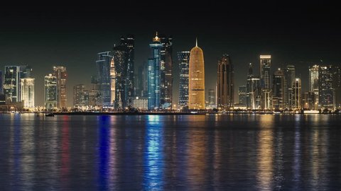 The skyline of Doha. Doha at night Time-lapse, Qatar. Wide shot, Modern skyscrapers and towers with the sea at night. Tall buildings city center Time-lapse video, Middle East.