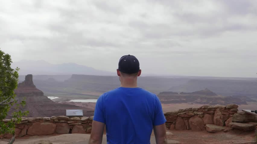 Following a man in a blue shirt walking up to an overlook at Dead Horse Point State Park in slow motion.