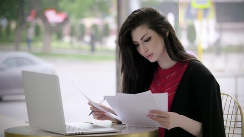 beautiful young girl in a business suit looking for a job fill out a form or resume looking at the laptop sit in a cafe. concept employment and crisis.