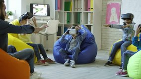 Playful little boys and girls sitting on colorful bean bag chairs, watching educational video in VR glasses and trying to touch holographic projection of Earth planet rotating in center of classroom
