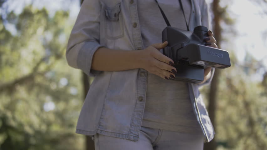 Girl walks through forest makes a photo at sunset. Active healthy Caucasian woman with a backpack taking pictures with an old film camera on a forest lake. 