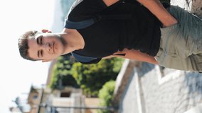 Vertical Video. Portrait of Attractive Male Teenager with Backpack Outdoors in Urban Environment Looking into the Camera. Tourism, Recreation, Education Concept. Ready for vertical video use