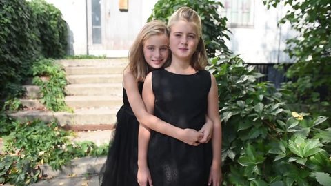 Pretty identical  twins girls in the black dress posing on camera. Beatiful children. Sisters love. Late summer early autumn. Shoot in august 2018