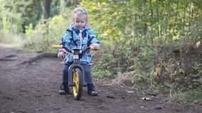 little girl rides a rattle in the autumn forest. The girl kicks and rolls forward. She smiles. Slow shooting. On the little girl wearing a jacket. Fun video