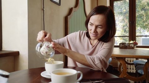 Happy woman in a cafe pours tea into a cup.