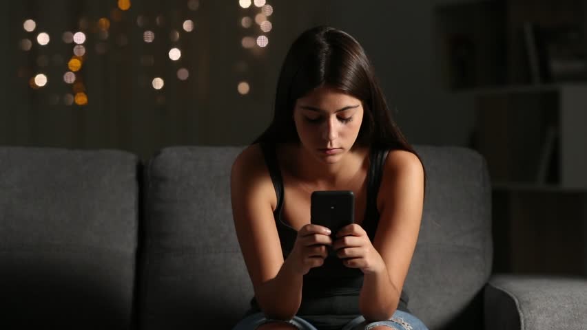 Front view of a sad girl reading cyber bullying phone message sitting on a couch in the night at home Royalty-Free Stock Footage #1017559864