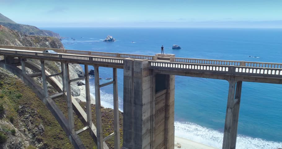 Aerial over person standing on Bixby Bridge. Big Bur Coastline and Highway One road in California, USA
