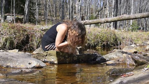Young woman enjoying nature on peaceful, calm Red Creek river in Dolly Sods, West Virginia during sunny day with reflection drinking fresh, splashing water from hands