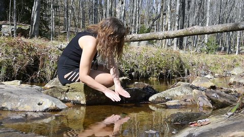 Young woman enjoying nature on peaceful, calm Red Creek river in Dolly Sods, West Virginia during sunny day with reflection dipping hands in water to drink fresh, splashing