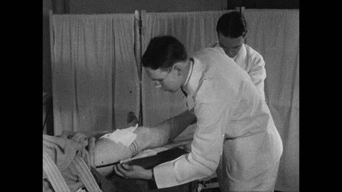 1930s: UNITED STATES: medics put man's leg in splint. Doctor bandages leg of patient.