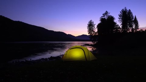 The yellow tent costs on the bank of the mountain lake. Night. In a tent light burns.