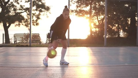 Close up footage of a young girl basketball player training and exercising outdoors on the local court. Young woman in white golf socks training cross bouncing with basketball ball