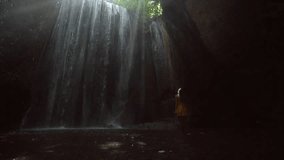 Girl in yellow dress walking happily in beautiful waterfall in Bali enjoying vacations in tropical rainforest climate. People travel dreamlike destinations concept- Slow motion