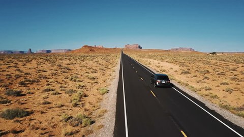Beautiful aerial shot of silver car driving along amazing American desert road towards mountains in Monument Valley. : vidéo de stock