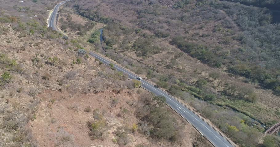 White van traveling along bend in road crossing rail tracks aerial tracking shot