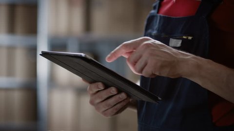 Close-up on a Man's Hands Using Digital Tablet Computer while Standing in the Warehouse.