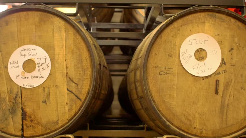Tracking shot of a rack of barrels holding various stouts and ales in a microbrewery