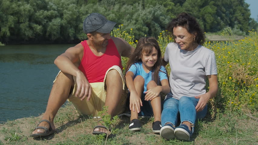 Happy family resting in nature. Parents with a daughter by the river.