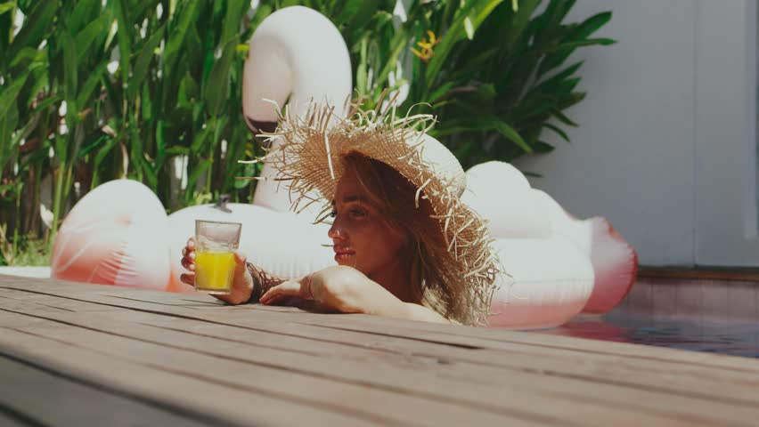 Young girl in straw hat in the pool drinking fresh squeezed juice. Conception of healthy lifestyle.