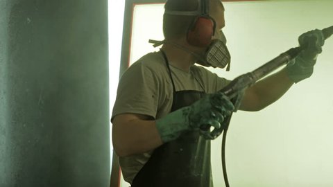 A man in a respirator and headphones reclaims a silk screen printing frame and removes emulsion