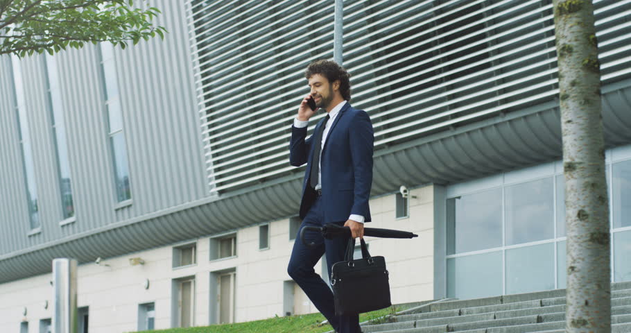Good looking Caucasian man in the business style stepping the stairs in the center of the town and having a conversation on the mobile phone.
