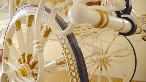 Big wheels on white baroque style horse carriage close-up 4K. Dolly slide shot of wheels in focus decorated with gold details.