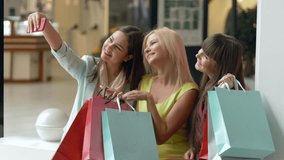 female shopaholism, joyful girlfriends take pictures on cell phone while shopping with packages in hands during sales season and discounts on black friday in mall