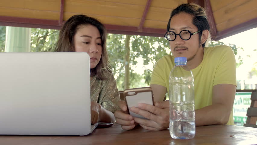Beautiful asian Woman Shows Interesting Stuff on Her Smartphone to Her Friends while They Have Good Time in garden . They Laugh, Joke .