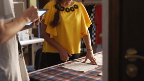 Fashion designer woman working in studio. Caucasian female tailor drawing the layout for clothes on cloth using chalk and ruler and teaching young student standing with tablet and sketching. - Powered by Shutterstock - Get 15% off with code: PIKWIZARD15